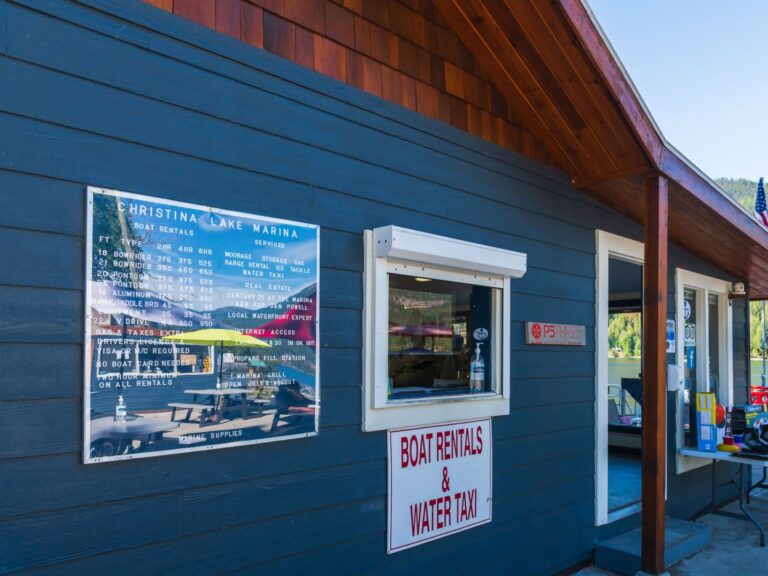 A blue marina building with a service window and a sign reading Boat Rentals & Water Taxi. A large price and information board, featuring watersports options, is mounted on the wall next to the window.