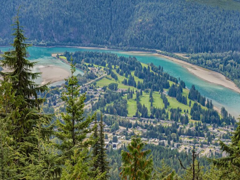 A scenic view from a hillside overlooks a small town surrounded by dense pine forests, with a winding turquoise river and sandy banks—a peaceful landscape perfect for quiet reflection or repeating your 7 affirmations.