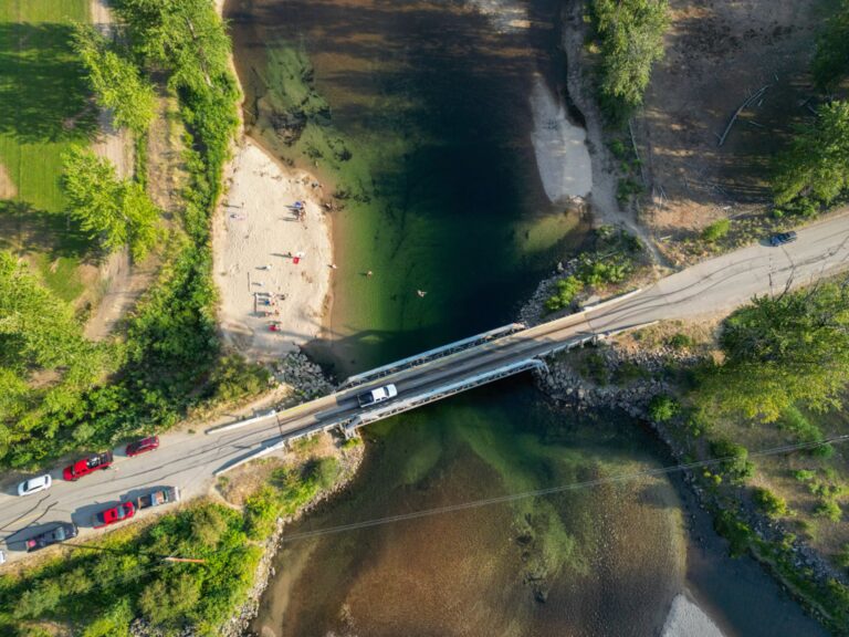 Overhead view of cars crossing a narrow bridge with a riverside beach below
