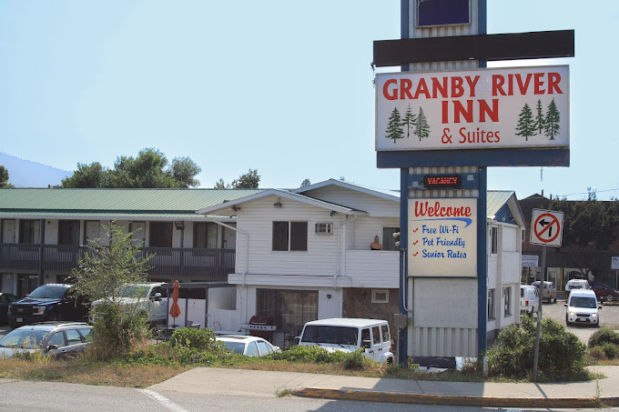 A roadside motel with a large sign reading Granby River Inn & Suites. The sign mentions free Wi-Fi, pet-friendly rooms, and seniors rates. Several vehicles are parked in front of the motel buildings.